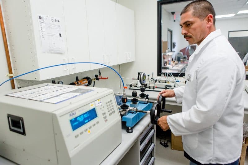 American Gage technician operating a hydraulic pressure comparator with a precision pressure controller in the pressure lab