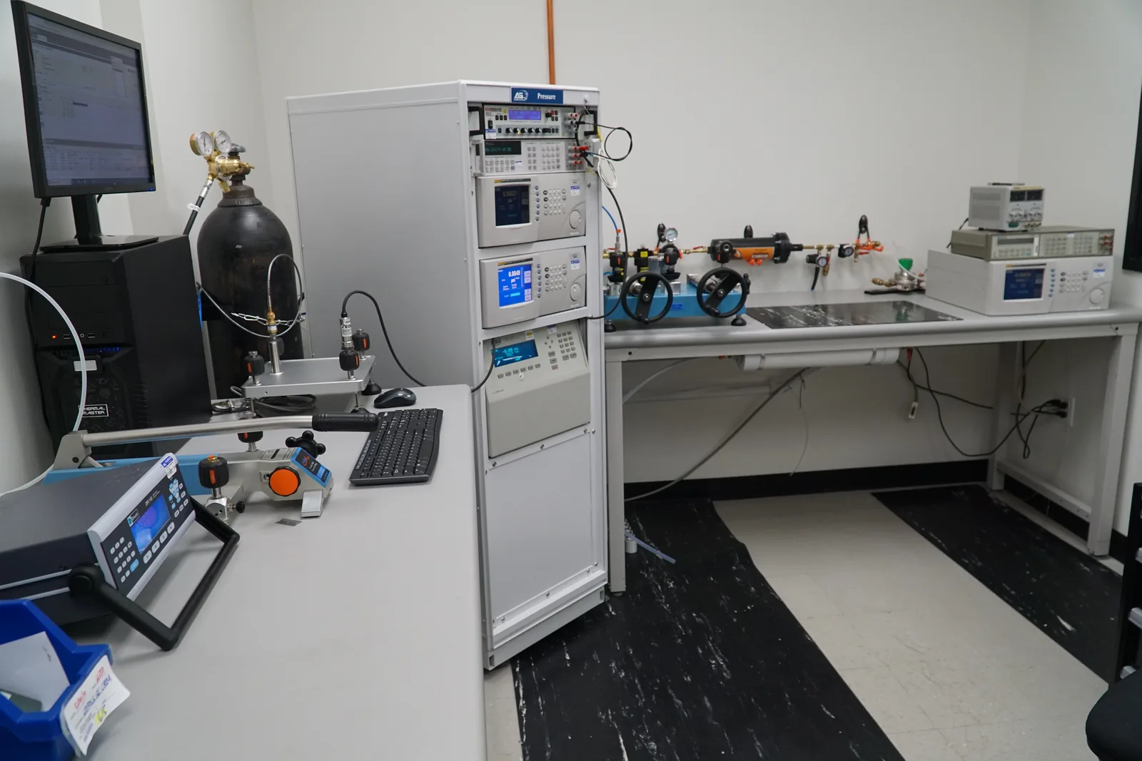 American Gage pressure calibration laboratory with rack-mounted pressure controllers, a hydraulic comparator bench, and nitrogen supply