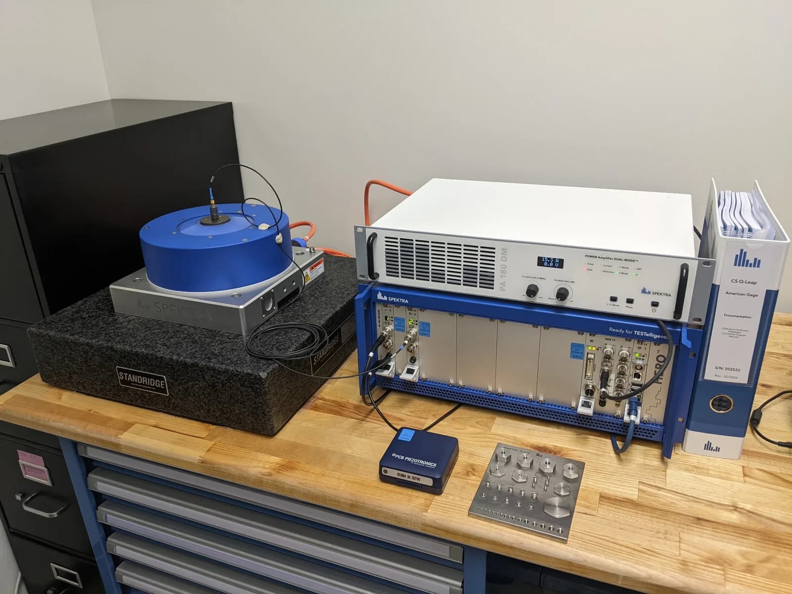 SPEKTRA vibration calibration system at American Gage: an electrodynamic shaker on a granite base with a PA 180 DM power amplifier, CS Q-Leap calibration system, and accelerometer mounting adapter plate